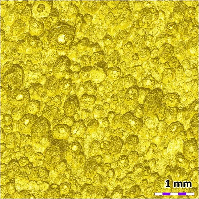 2D photo simulation of the yellow climbing grip surface showing pores, roughness, and morphology under artificial lighting.